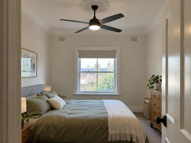 Bedroom with a black ceiling fan and light above a made bed in a cream room in The Junction